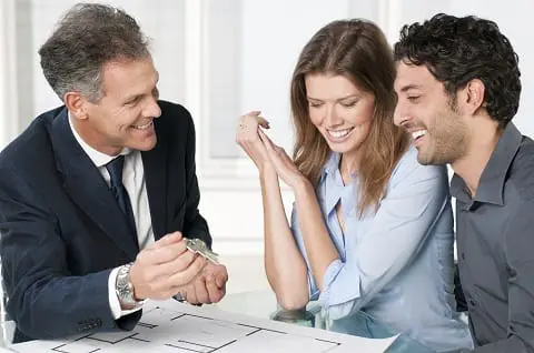 Happy estate agent showing new home keys to a young couple after a discussion on house plans.