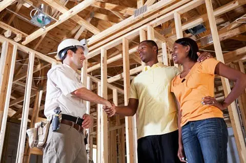 African American couple (20s) standing in house under construction talking with builder (30s).