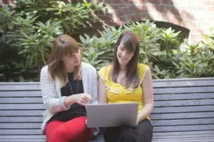 Two women on a bench looking at a laptop.