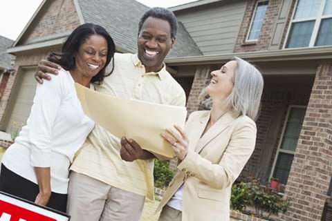 Senior couple signing paperwork wtih realtor outside recently sold home